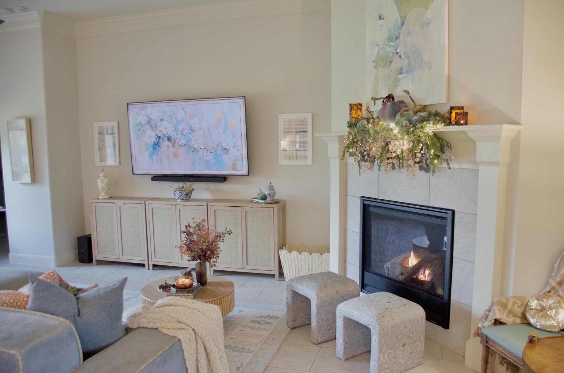 Living room with blue upholstery, patterned rug, seasonal coffee-table arrangement, and a fireplace mantel decorated with velvet pumpkins and trailing greenery.